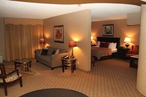 Habitación de hotel con sofá, cama, escritorio y silla. Hay lámparas en el escritorio y en las mesitas de noche.