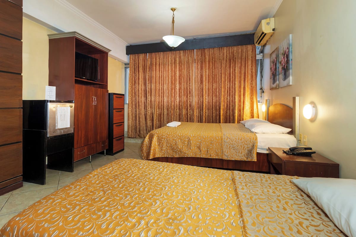 Une chambre d’hôtel avec deux lits, une armoire, un bureau avec un téléphone et un tableau au mur.