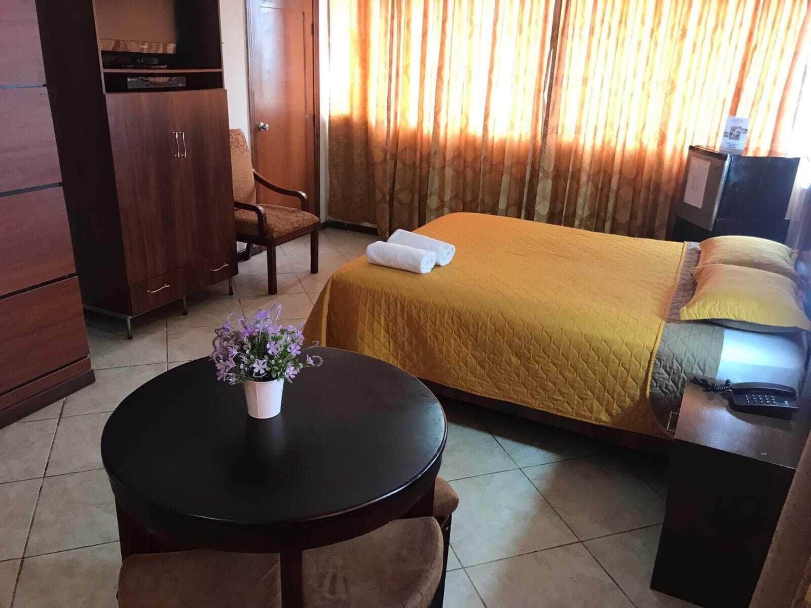 Habitación de hotel con cama, escritorio, silla, una mesita con un florero y teléfono.