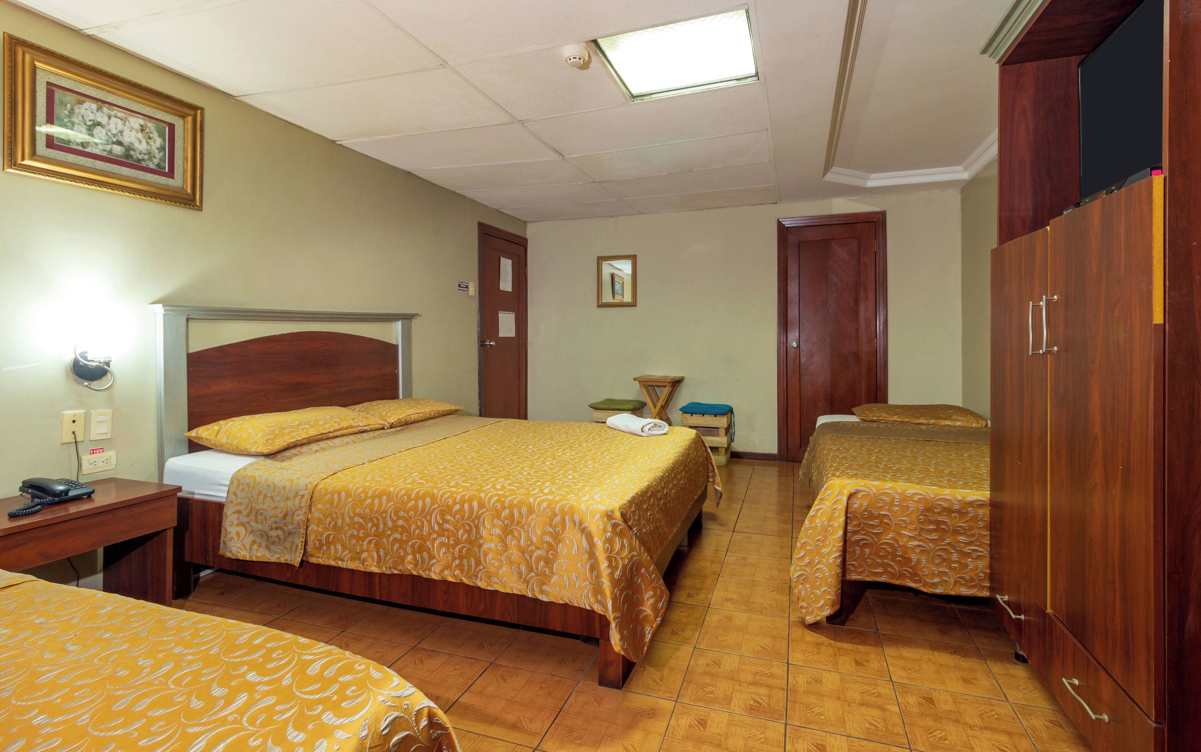 Habitación de hotel con dos camas, un escritorio, una silla, un armario y un espejo en la pared.