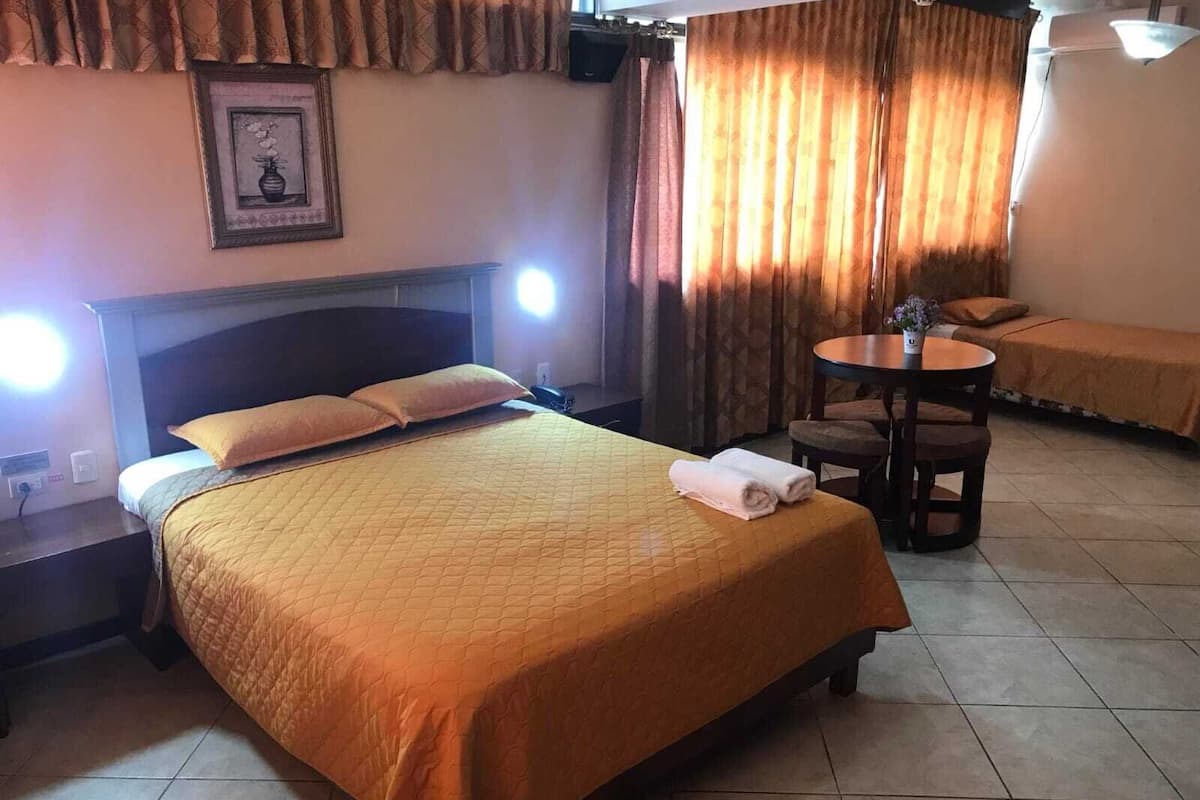 Une chambre d’hôtel avec un lit, une table de chevet, une chaise, une petite table avec une lampe et des rideaux.