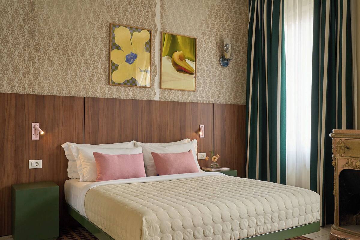 A neatly made bed with a quilted cover, a green nightstand, and a wall-mounted light fixture.