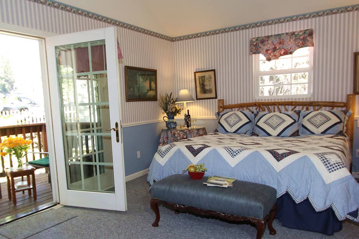 A bedroom with a large bed, a wooden bench, a door leading to a balcony, and a window with floral curtains.