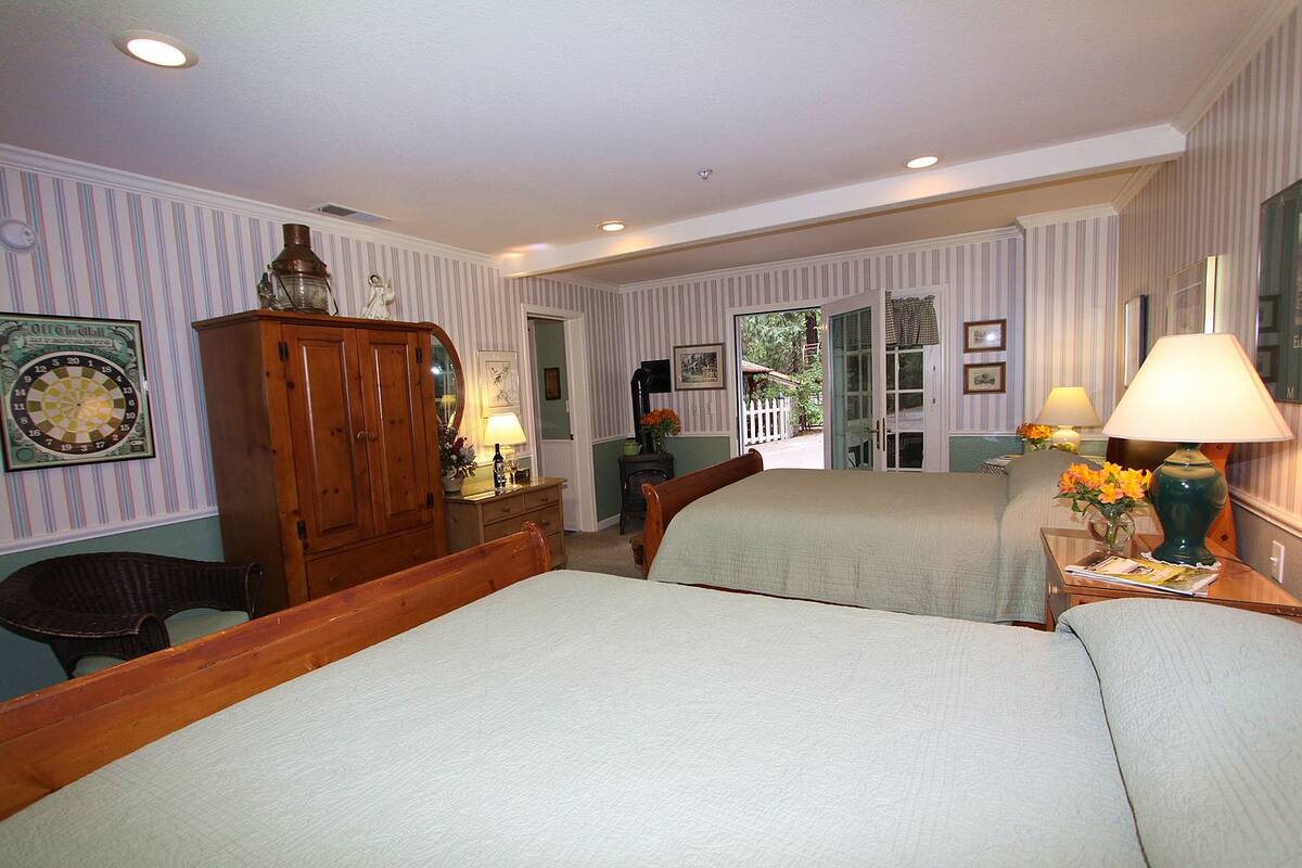 A hotel room with two beds, a wooden wardrobe, a desk with a lamp, and a view of the outside.