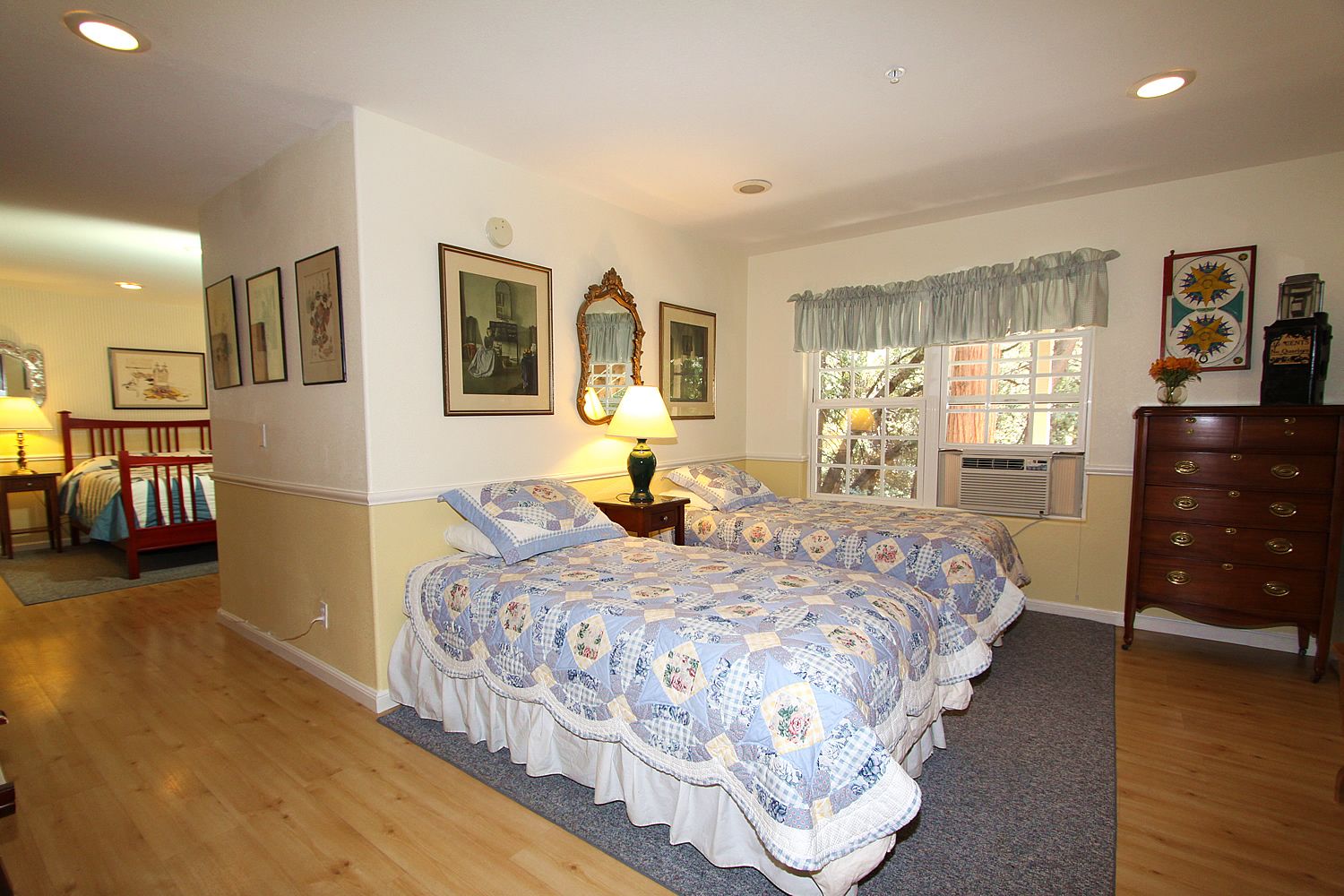 Une chambre avec deux lits, une commode, un miroir et des œuvres d’art encadrées accrochées aux murs.