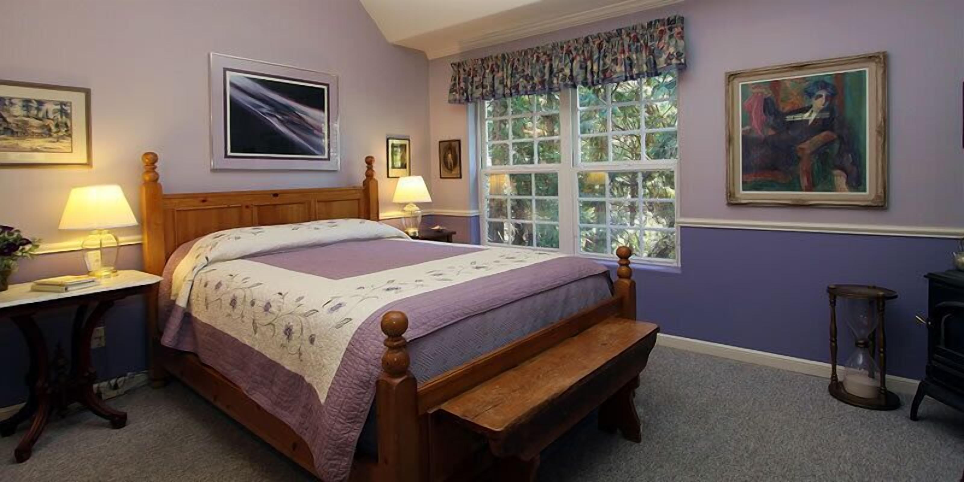 A bedroom with a wooden bed, two bedside tables, a bench, a window with a view, and a painting on the wall.
