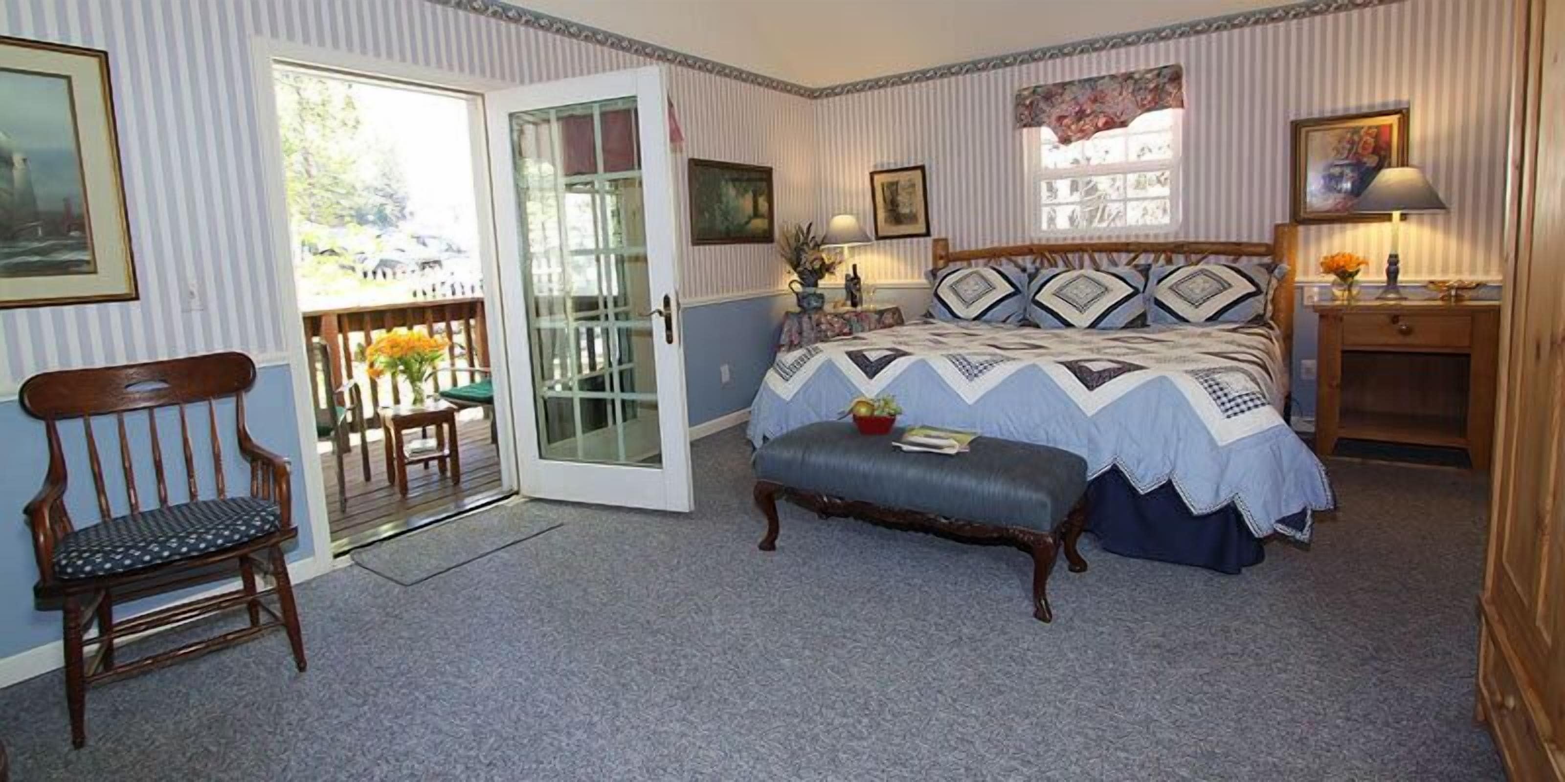A bedroom with a bed, a bench, a chair, and a door leading to a balcony.