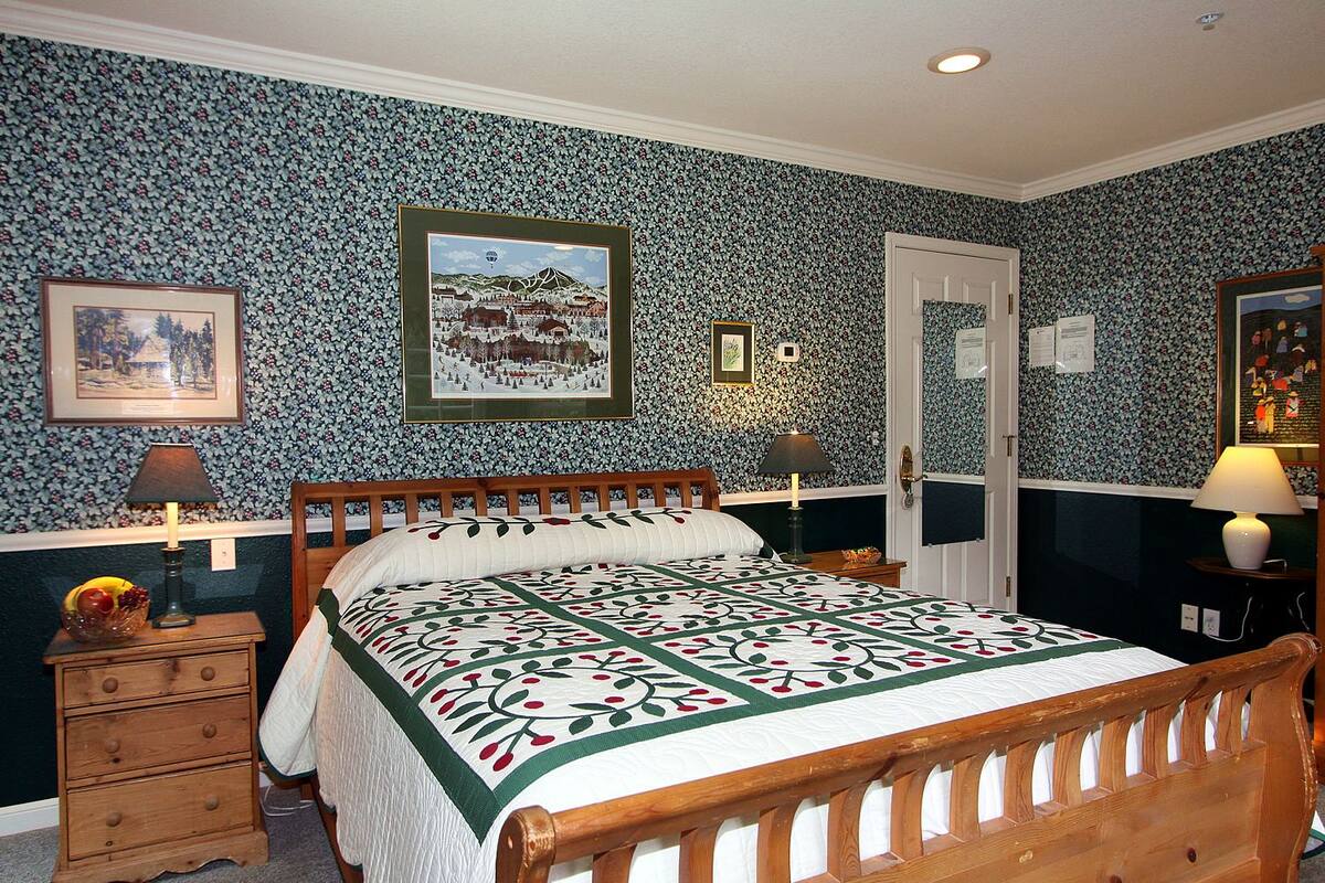 A bedroom with a wooden bed, floral wallpaper, and framed pictures on the walls.