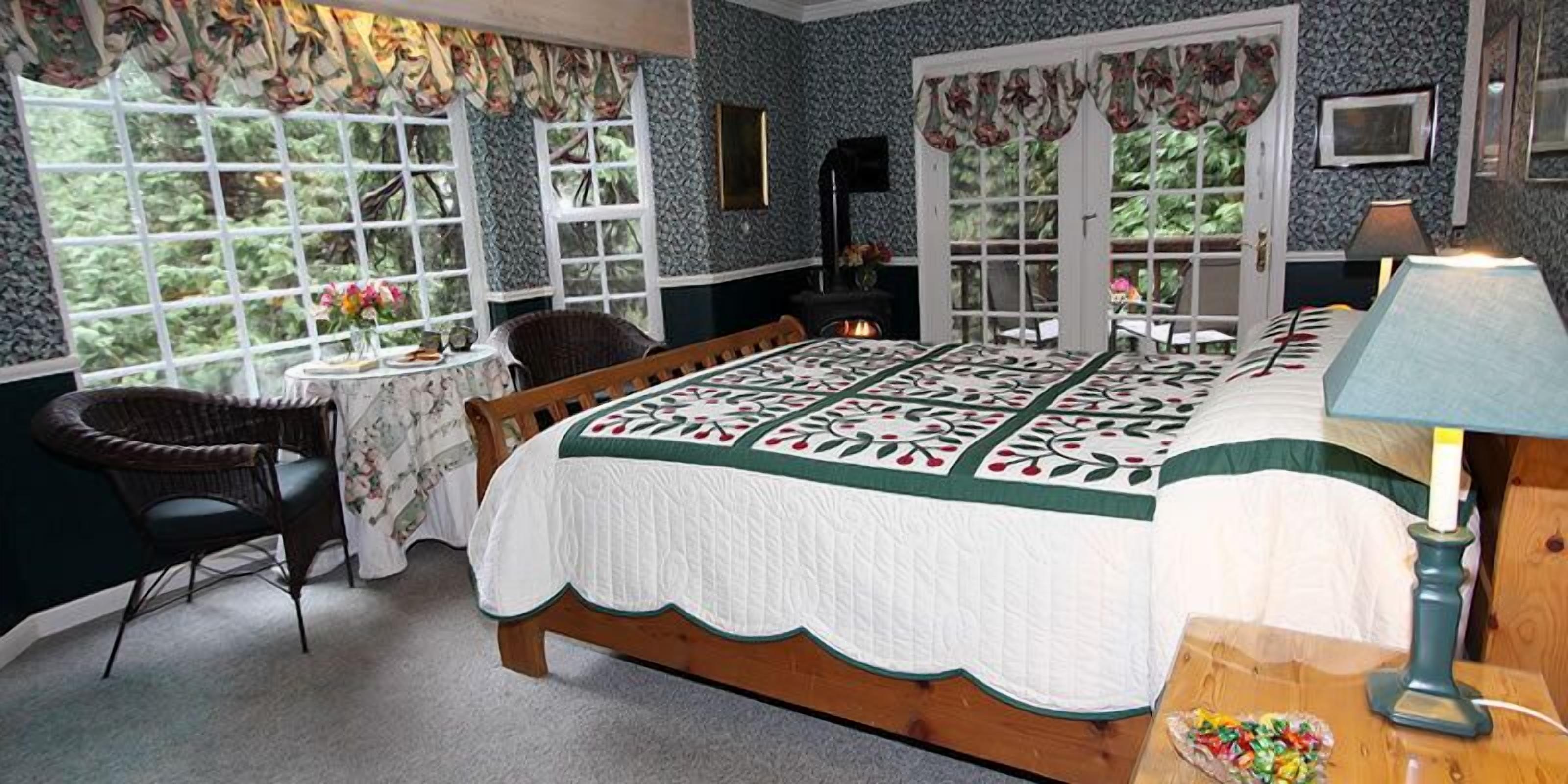 A bedroom with a large bed, a chair, a small table with a vase, and a fireplace.