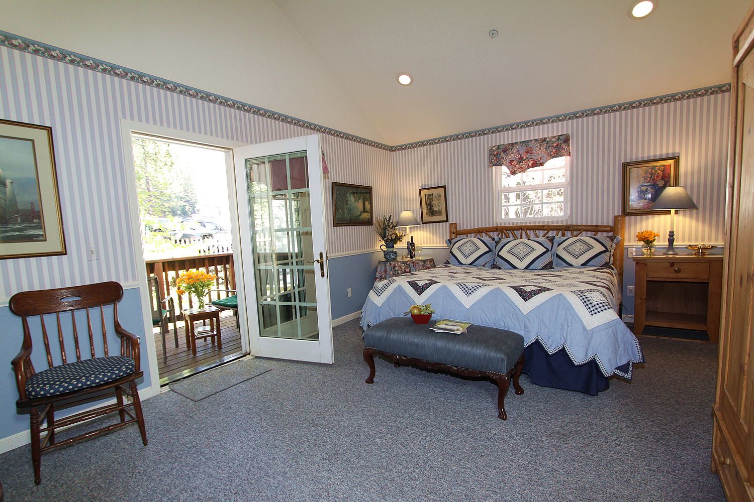 A bedroom with a large bed, a wooden chair, a desk, and a balcony with a view.