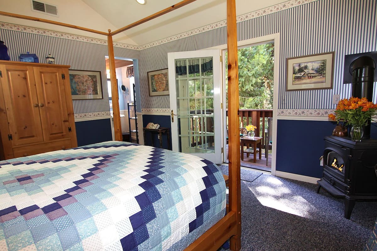 A bedroom with a four-poster bed, a wooden wardrobe, a fireplace, and a view of the outdoors.