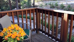Una terraza de madera con una silla y una mesa, rodeada por un cercado blanco de piquetes y árboles.