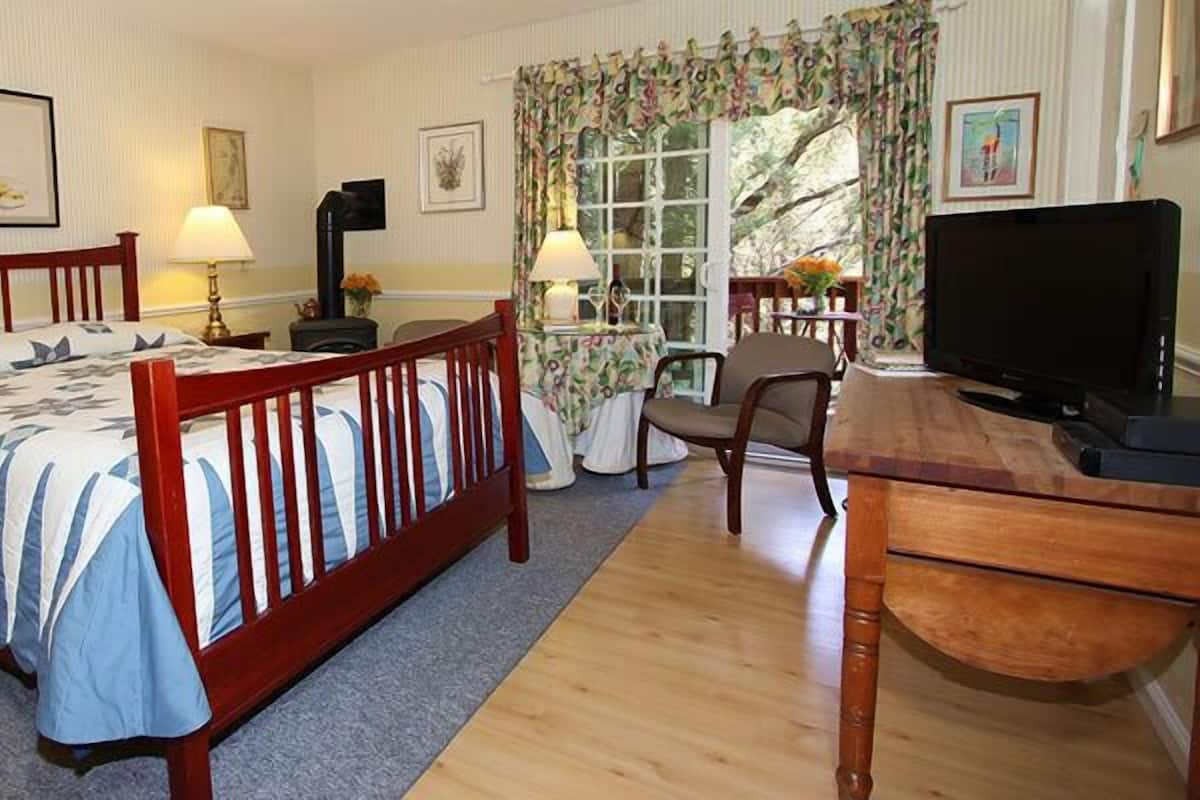 A bedroom with a wooden bed, bedside tables, a desk, a television, and a window with curtains.