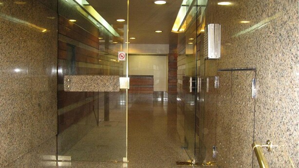 Une entrée moderne avec des portes en verre, un panneau indiquant qu’il est interdit de fumer et un portail de sécurité en métal.