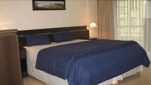 Une chambre d’hôtel avec un grand lit, une table de chevet, une lampe et une fenêtre avec des rideaux.