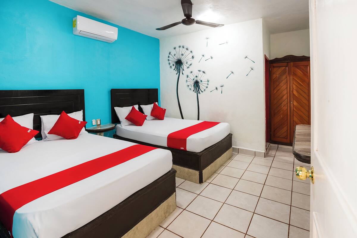 Habitación de hotel con dos camas, ventilador de techo, aire acondicionado y armario de madera.