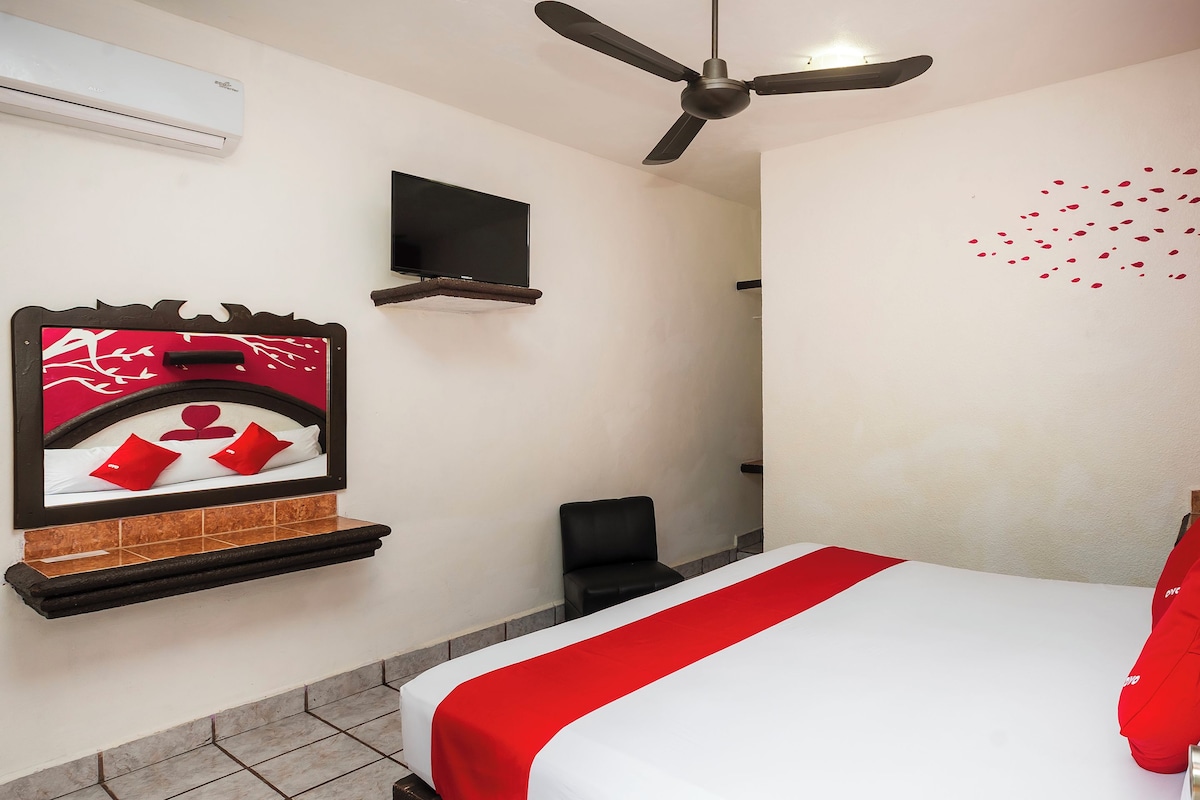 A hotel room with a bed, a TV, a ceiling fan, and a wall-mounted shelf.