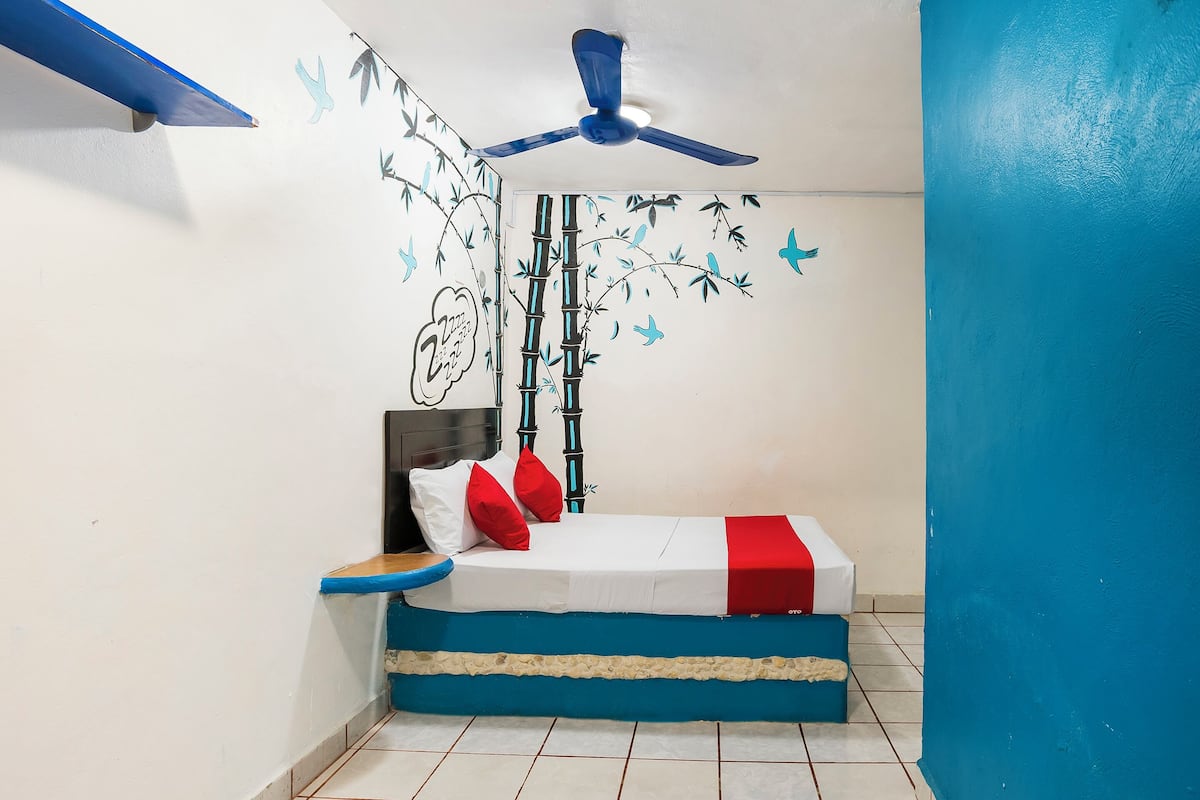 Un dormitorio con cama, ventilador de techo, pared con un mural de bambú y mariposas, y una pared azul decorativa.