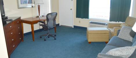 A hotel room with a desk, two chairs, a sofa, a dresser, and a window with curtains.