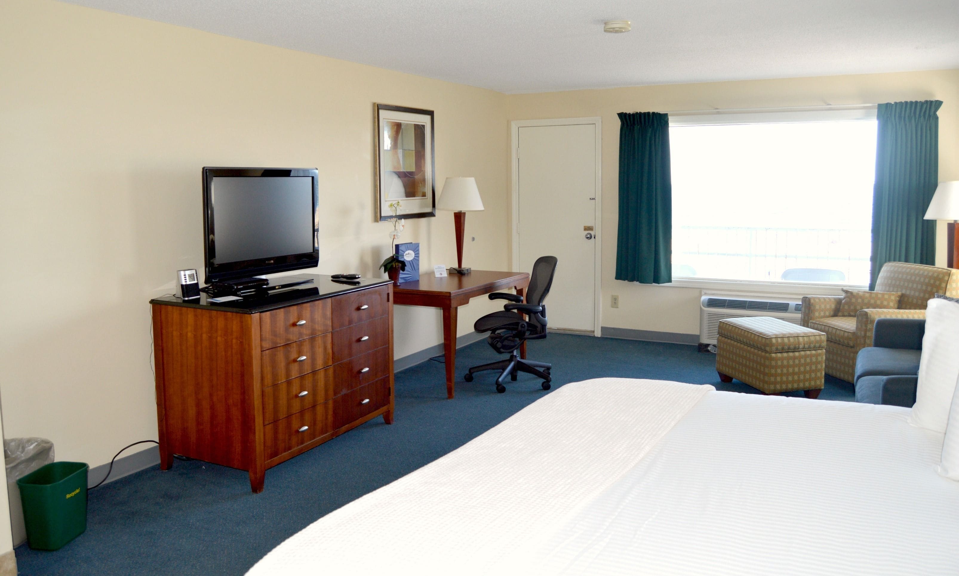 Une chambre d’hôtel comprenant un lit, un bureau avec une chaise, une télévision et une fenêtre avec des rideaux.