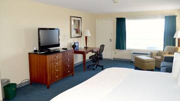Une chambre d’hôtel comprenant un lit, un bureau avec une chaise, une télévision et une fenêtre avec des rideaux.