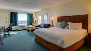 A hotel room with a large bed, a desk, a chair, a sofa, and a view of the ocean. - Hampton House Hotel (Hampton)