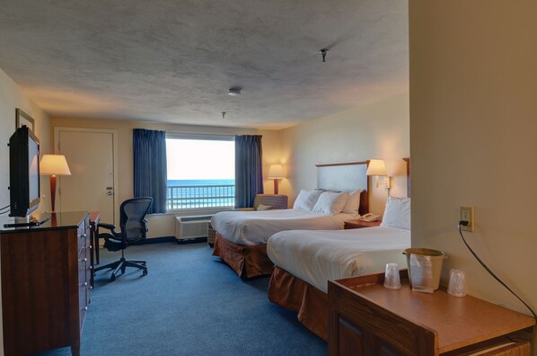 A hotel room with two beds, a desk, a chair, and a window with curtains.