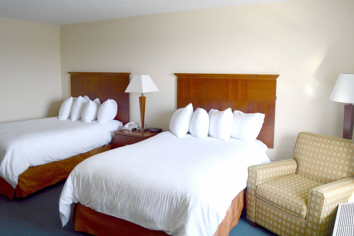 Une chambre d’hôtel avec deux lits, une chaise et une table de chevet avec une lampe.