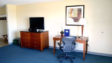 Habitación de hotel con un aparador de madera, un escritorio con una silla, un televisor, un cuadro en la pared y una lámpara.