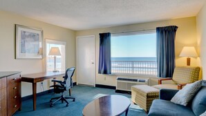 A hotel room with a desk, office chair, sofa, and a view of the beach. - Hampton House Hotel (Hampton)