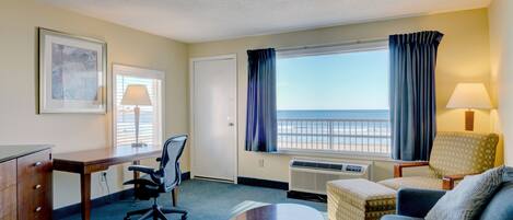 Een hotelkamer met een bureau, bureaustoel, bank en uitzicht op het strand.