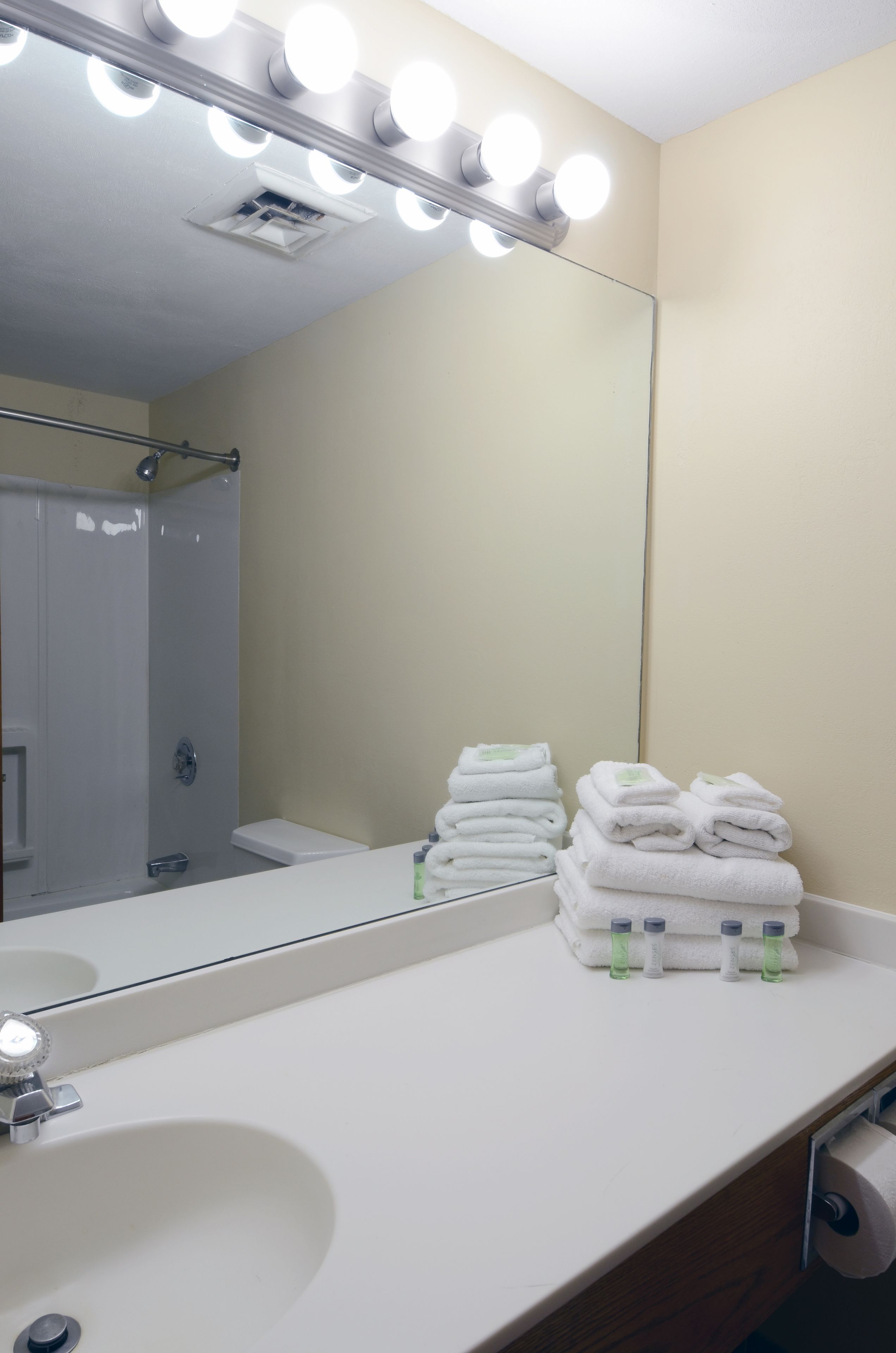 A bathroom with a large mirror, white sink, and stacked towels.