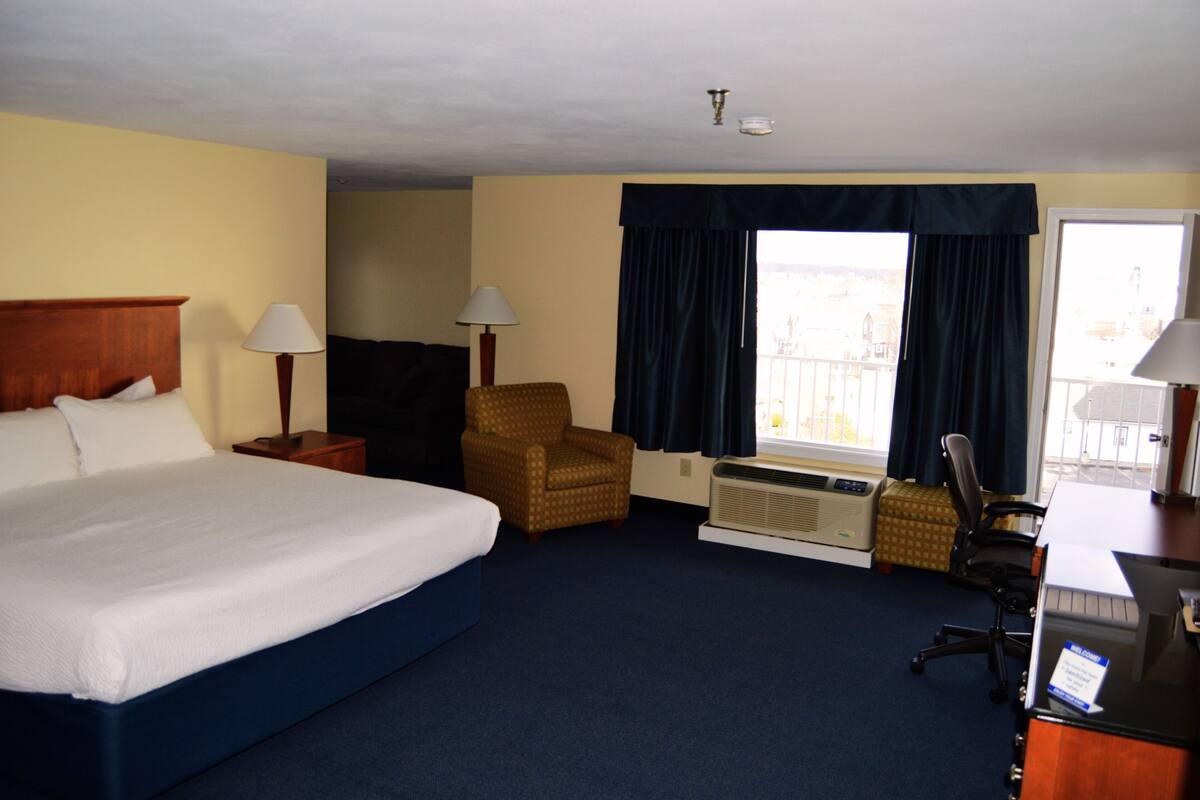 Une chambre d’hôtel avec un grand lit, une chaise, un bureau et une fenêtre avec des rideaux.
