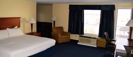 Una habitación de hotel con una cama grande, una silla, un escritorio y un ventanal con cortinas.