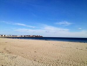 A wide sandy beach with a clear blue sky and a distant shoreline with buildings. - Hampton House Hotel (Hampton)