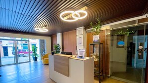 Et hotellets receptionområde med et moderne design, der inkluderer en receptionsdisk, en glasdør indgang og et træloft.