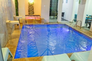 A rectangular indoor pool with clear blue water, surrounded by stone tiles and a small waterfall feature.