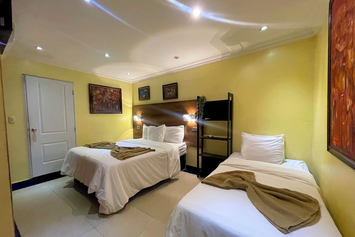A hotel room with two beds, a door, a wall-mounted shelf, and a painting.