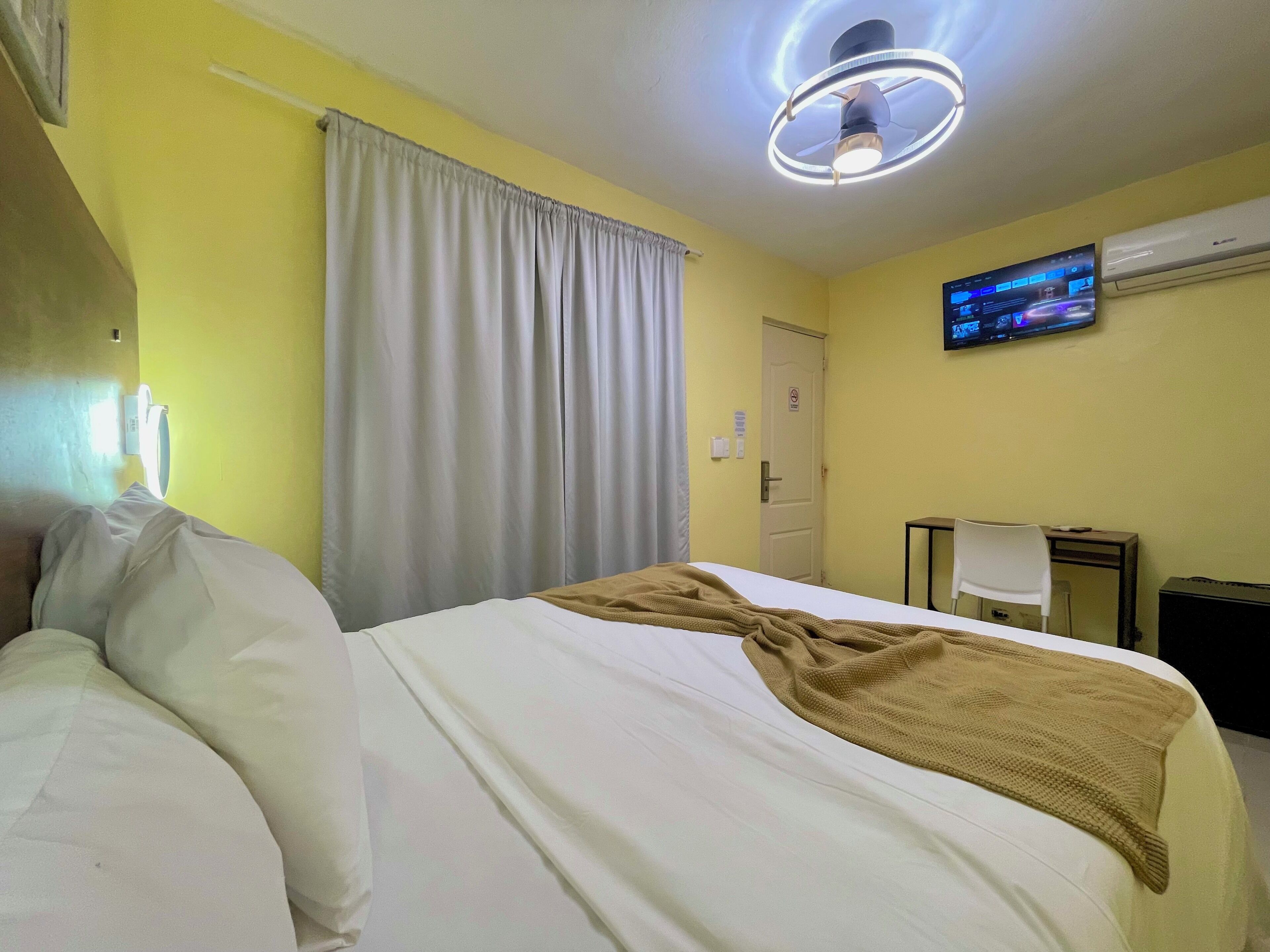 A hotel room with a bed, a TV mounted on the wall, and an air conditioning unit.