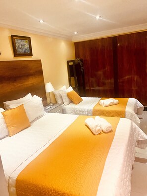 A hotel room with two beds, each with white linens and orange accents, a wooden headboard, a painting on the wall, and a large window with a view.