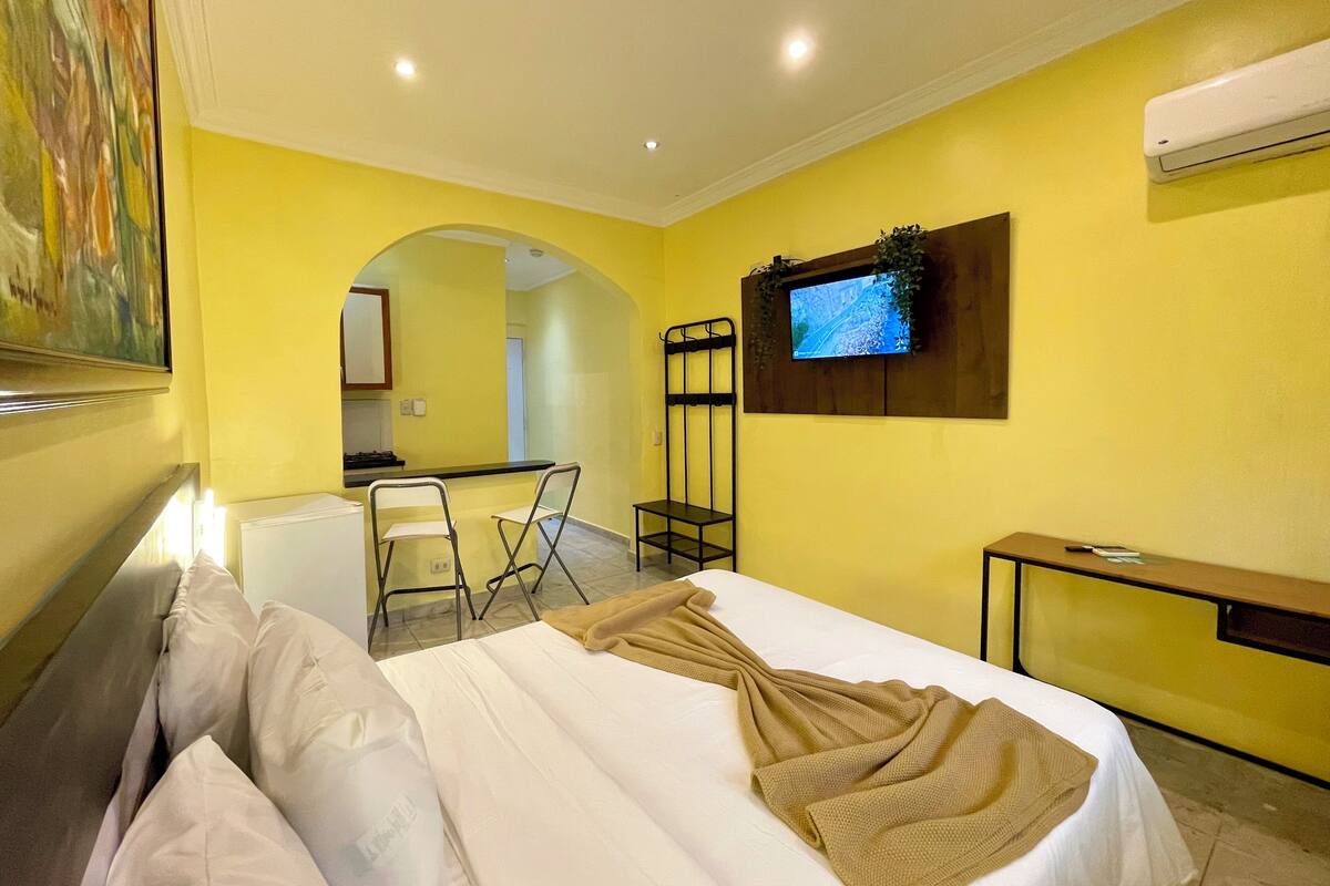 A hotel room with a bed, a TV mounted on the wall, a desk, and a chair.