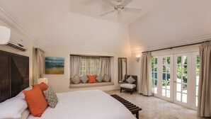 A bedroom with a large bed, a window seat, a ceiling fan, and a view of the outdoors. - Green Monkey Villa (Holetown)
