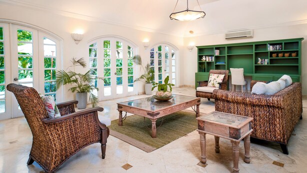 A spacious living room with wicker furniture, a glass coffee table, and a green bookshelf. - Green Monkey Villa (Holetown)