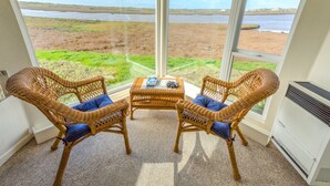 A room with two wicker chairs and a small table, large windows with a view of a beach and water. - Captain's Inn at Moss Landing (Moss Landing)