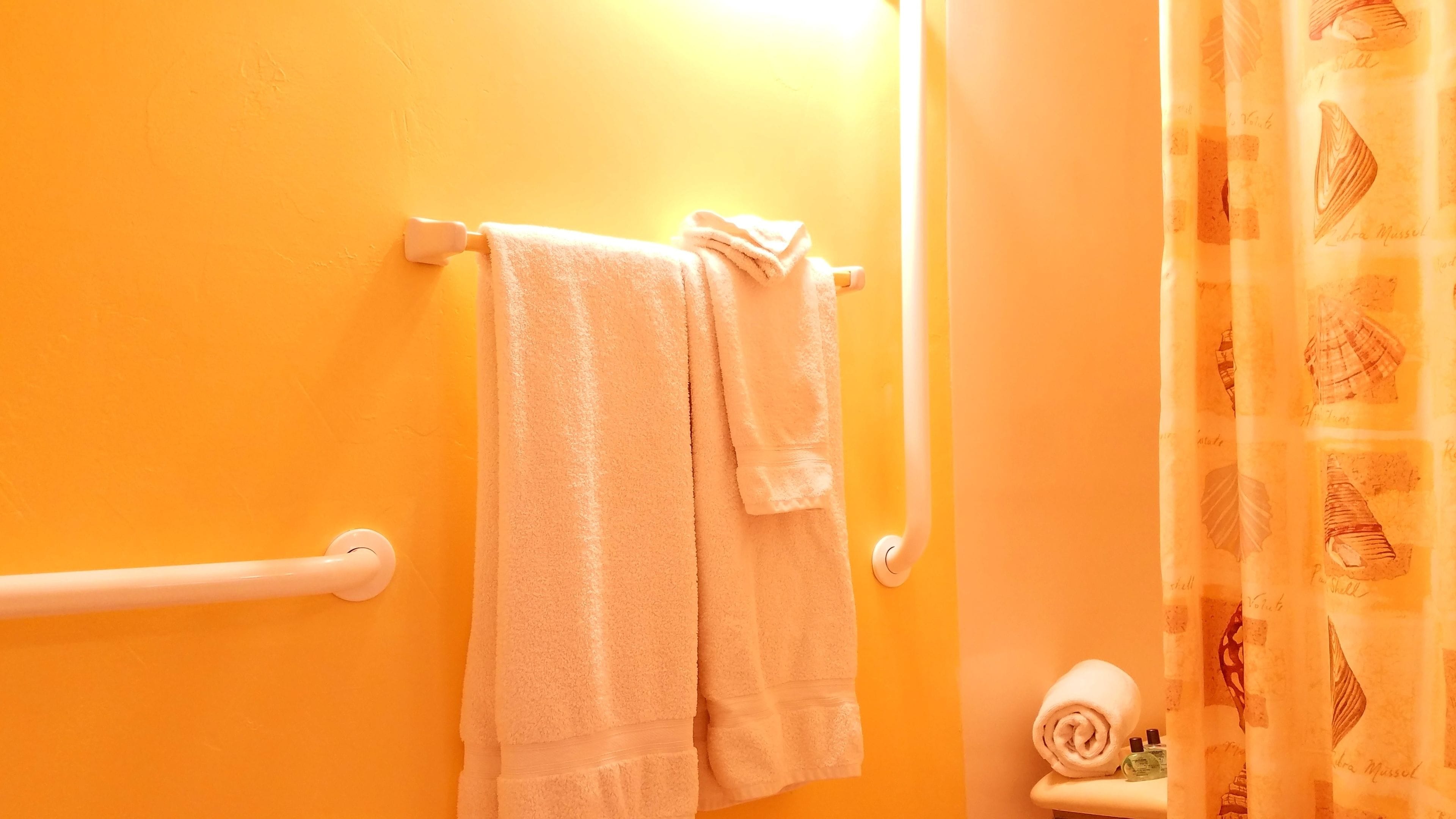 A bathroom with an orange wall, a towel rack with two towels, a handrail, and a toilet with a patterned shower curtain.