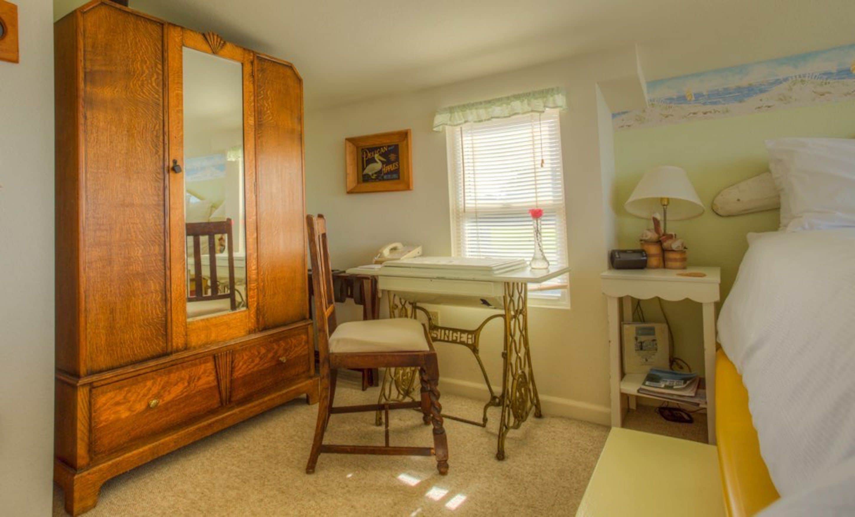 Une chambre avec une armoire en bois, un bureau avec une chaise, un lit et une fenêtre avec des stores.