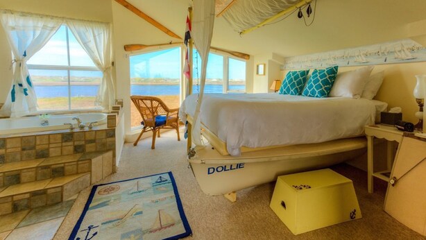 A bedroom with a bed, a window with curtains, a chair, and a small table. - Captain's Inn at Moss Landing (Moss Landing)