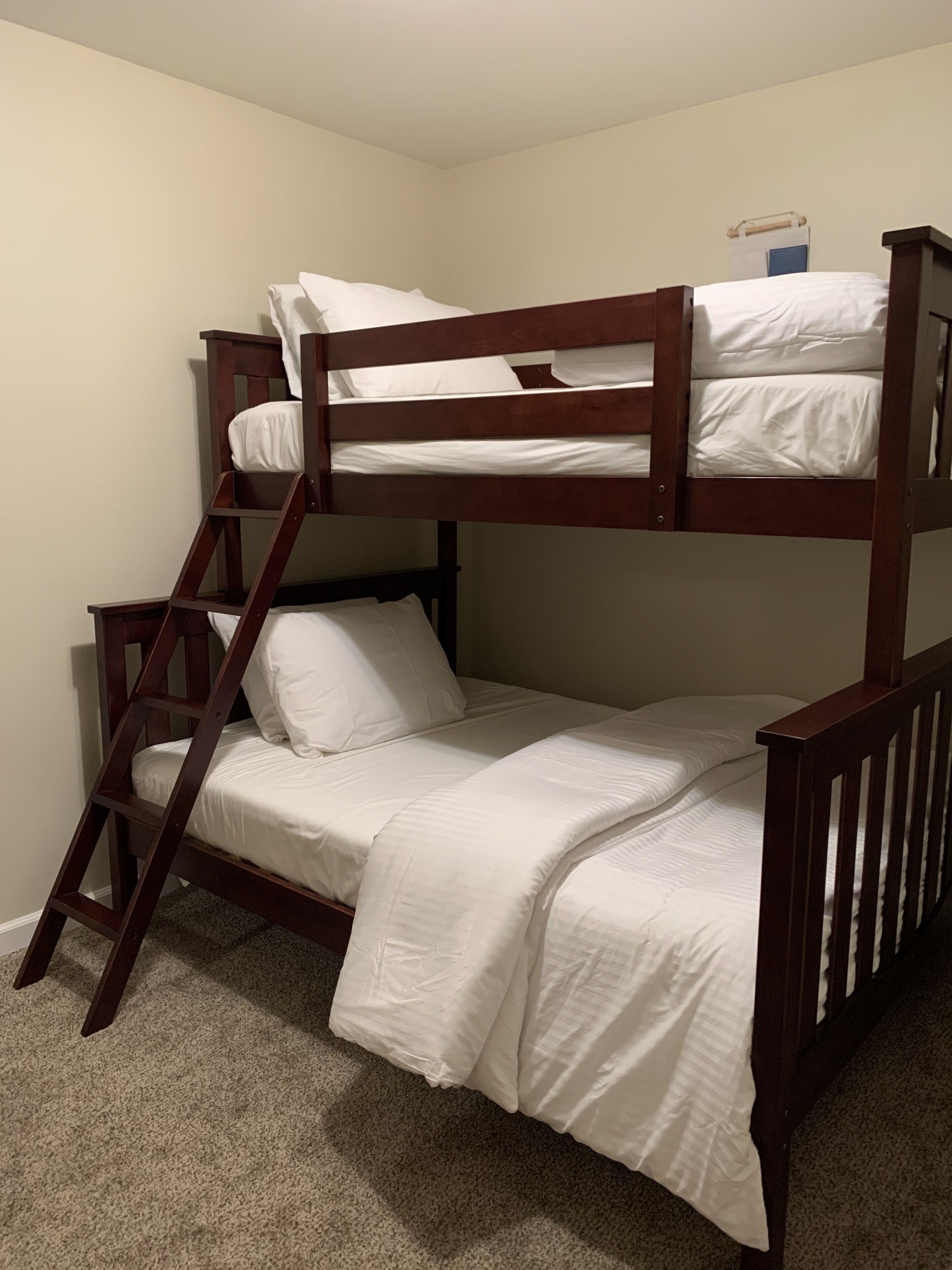 A bunk bed with a wooden ladder and white bedding.