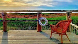 A wooden deck with a rope barrier, a lifebuoy, and a wicker chair overlooking a water body. - Captain's Inn at Moss Landing (Moss Landing)