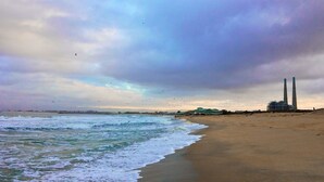 A beach with waves, a distant industrial structure, and a cloudy sky. - Captain's Inn at Moss Landing (Moss Landing)